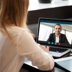 Adult sitting at a desk having a video call with another individual on a laptop.
