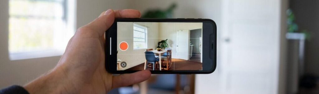 Smartphone held in one hand recording a dining room setup.