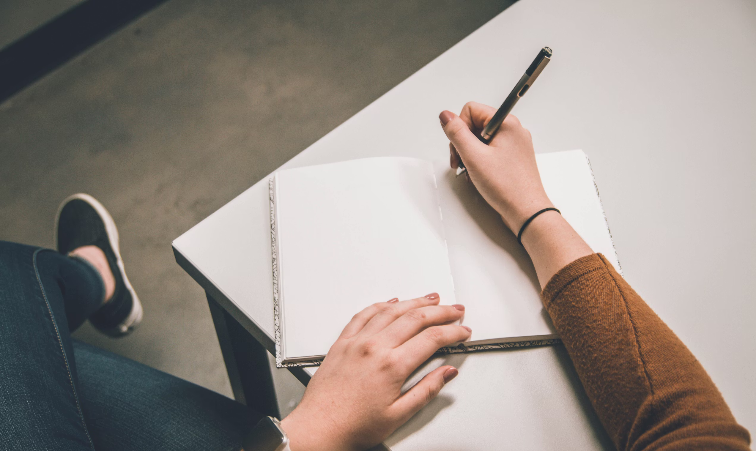 Notebook resting on a table being written in with a pen.